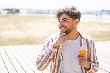 Açık havada kornet dondurması olan yakışıklı bir Arap bir fikir üretiyor ve bakıyor.