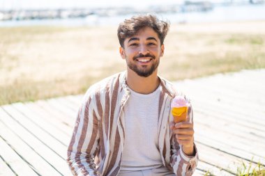 Açık havada bol bol gülümseyen kornet dondurmalı yakışıklı bir Arap.