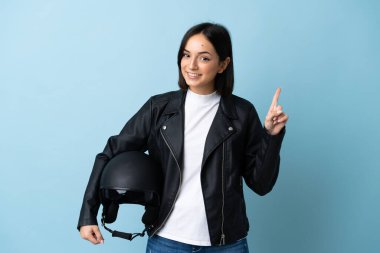 Mavi arka planda izole edilmiş motosiklet kaskı tutan kadın en iyinin işareti olarak parmağını kaldırıyor.