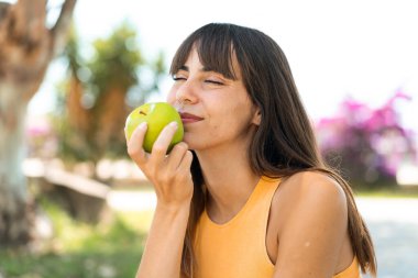 Dışarıda elinde elma tutan genç bir kadın.