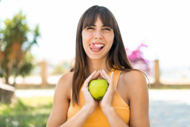 Açık havada elinde mutlu bir ifadeyle elma tutan genç bir kadın.