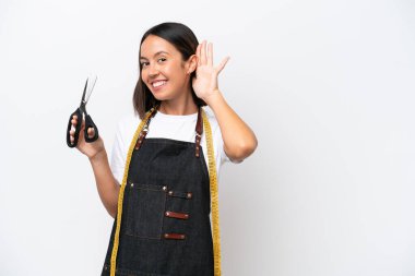 Genç terzi kadın, beyaz arka planda izole edilmiş bir şekilde elini kulağına koyarak bir şeyler dinliyor.