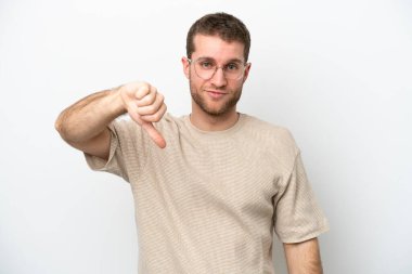 Beyaz arka planda izole genç beyaz adam olumsuz ifade ile baş parmağını göstermektedir