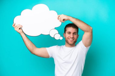 Young caucasian man isolated on blue background holding a thinking speech bubble