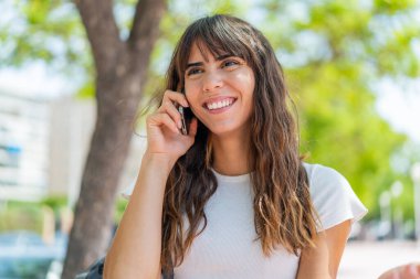 Açık havada cep telefonu kullanan genç bir kadın.