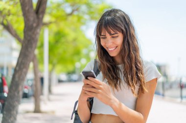 Açık havada cep telefonu kullanan genç bir kadın.