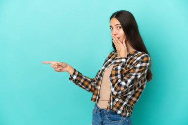 Mavi arka planda izole edilmiş genç bir Fransız kadını işaret ederken sürpriz bir ifadeyle