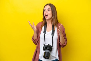 Genç fotoğrafçı beyaz kadın, sarı arka planda izole edilmiş, şaşırmış bir yüz ifadesi var.