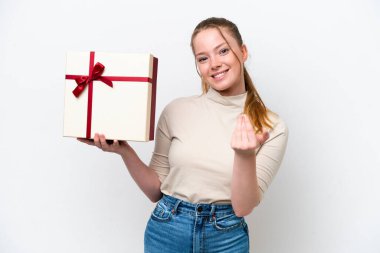 Beyaz arka planda izole edilmiş beyaz bir hediye tutan genç beyaz bir kadın bizimle gelmesi için davet ediyor. Gelmene sevindim.