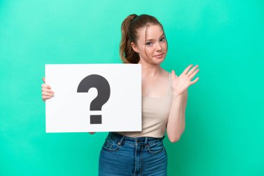 Kafkasyalı genç bir kadın yeşil arka planda izole edilmiş. Elinde soru işareti olan bir levha var ve dur işareti yapıyor.