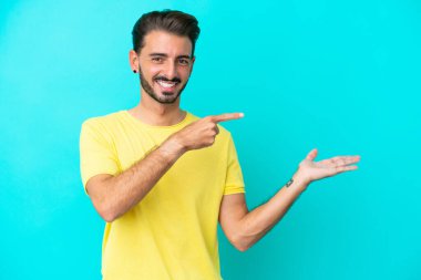 Mavi arka planda izole edilmiş genç beyaz adam bir ilan vermek için avucunun içinde hayali bir fotokopi makinesi tutuyor.