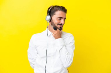 Tele pazarlamacı beyaz adam sarı arka planda izole edilmiş bir kulaklıkla çalışıyor.