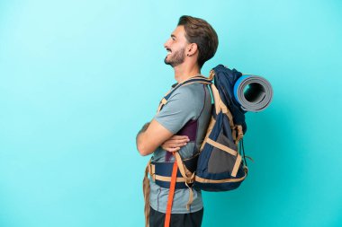 Mavi arka planda büyük bir sırt çantası olan genç dağcı yan pozisyonda izole edildi.