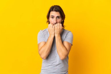 Sarı arka planda izole edilmiş genç yakışıklı gergin ve korkmuş, elleriyle suni teneffüs yapıyor.