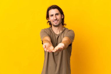 Sarı arka planda izole edilmiş genç yakışıklı bir adam. Avucunun içinde hayali bir ilan tutuyor.