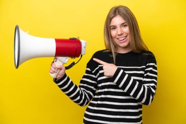 Sarı arka planda izole edilmiş genç beyaz bir kadın elinde bir megafon ve işaret eden bir kenar tutuyor.