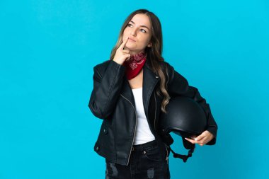 Mavi arka planda izole edilmiş motosiklet kaskı tutan Romen kadın, yukarı bakarken şüpheye düşüyor