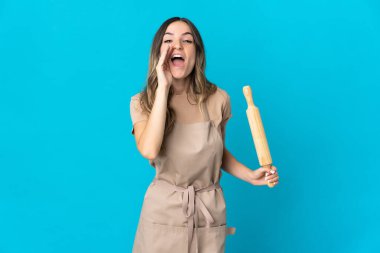 Romen genç bir kadın mavi arka planda izole edilmiş merdaneyi tutuyor ve ağzı açık bağırıyor