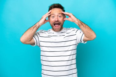 Orta yaşlı, beyaz bir adam mavi arka planda, sürpriz bir ifadeyle izole edilmiş.