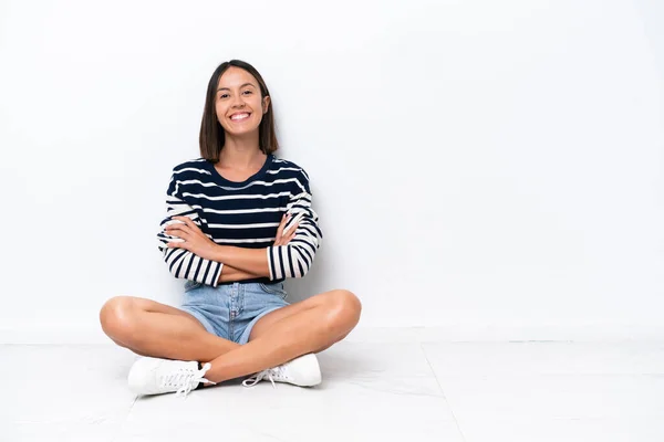 Young caucasian woman sitting on the floor isolated on white background keeping the arms crossed in frontal position