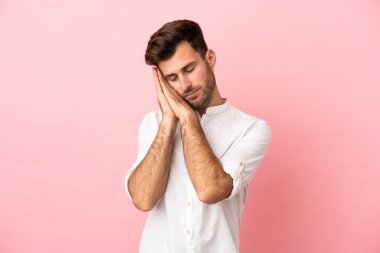 Pembe arka planda izole edilmiş beyaz, yakışıklı genç bir adam uyku jesti yapıyor.