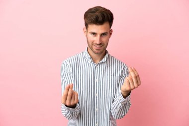 Beyaz tenli yakışıklı adam pembe arka planda izole edilmiş para hareketi yapıyor.