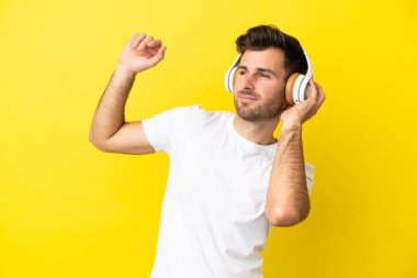 Beyaz tenli yakışıklı adam sarı arka planda izole edilmiş müzik ve dans dinliyor.