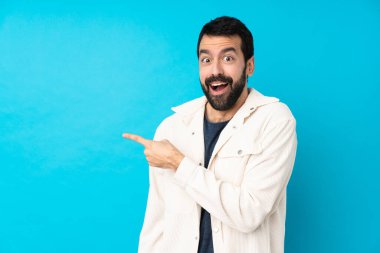 Mavi arka planda beyaz kadife ceketli yakışıklı genç adam şaşırmış ve işaret ediyor.