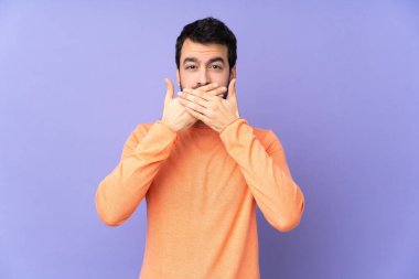 İzole edilmiş mor arka planı olan beyaz, yakışıklı bir adam elleriyle ağzını kapatıyor.