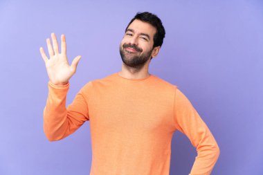 Kafkasyalı yakışıklı adam izole edilmiş mor arka planda mutlu bir ifadeyle selam veriyor.