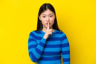 Young Chinese woman isolated on yellow background showing a sign of silence gesture putting finger in mouth