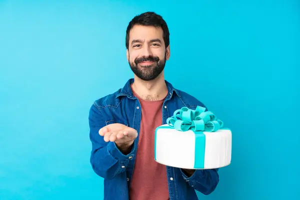Young handsome man with a big cake over isolated blue background holding copyspace imaginary on the palm to insert an ad