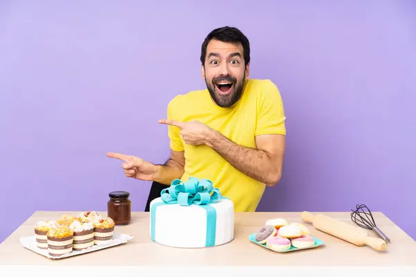 Man in a table with a big cake surprised and pointing side
