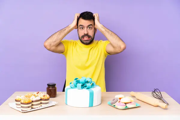 Man in a table with a big cake frustrated and takes hands on head