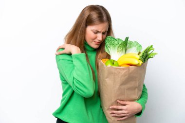 Beyaz arka planda izole edilmiş alışveriş torbası tutan beyaz bir kadın omuz ağrısından muzdarip.