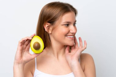 Beyaz arka planda izole edilmiş beyaz bir kadın elinde bir avokado tutarken gülümsüyor. Portreyi kapat