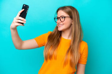 Mavi arka planda izole edilmiş beyaz bir kadın selfie çekiyor.