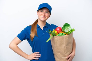 Genç teslimatçı kadın beyaz arka planda izole edilmiş bir paket yiyecek alıyor. Kolları kalçasında ve gülümsüyor.