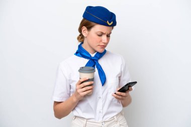 Uçak hostesi kadın beyaz arka planda izole edilmiş. Elinde kahve ve cep telefonu var.
