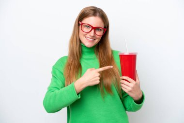 Young caucasian woman drinking soda isolated on white background pointing to the side to present a product