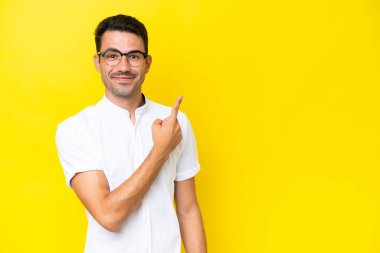 Soyutlanmış sarı arka planda genç yakışıklı bir adam bir ürün sunmak için kenarı işaret ediyor.