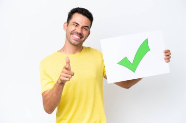 İzole edilmiş beyaz arka plan üzerinde genç yakışıklı bir adam elinde yeşil işaret simgesi olan bir pankart tutuyor ve ön tarafı işaret ediyor.