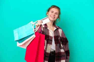 Mavi arka planda izole edilmiş genç bir İngiliz kadın elinde alışveriş çantaları ve bir kredi kartı tutuyor.