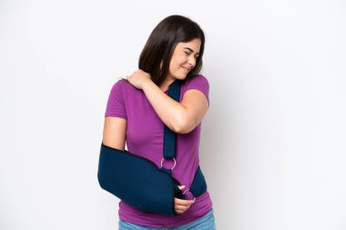 Kırık kollu, beyaz arka planda askısı olan, omuz ağrısı çeken genç Brezilyalı bir kadın çabaladığı için acı çekiyor.