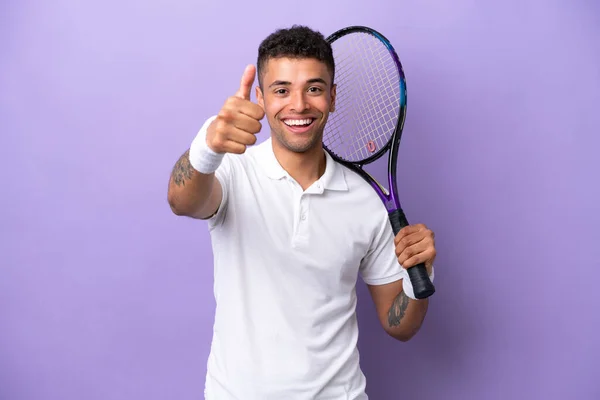Young Brazilian man isolated on purple background playing tennis and with thumb up