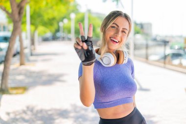 Açık havada gülümseyen ve zafer işareti gösteren genç, güzel spor kadın.