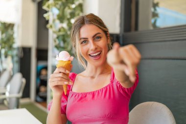 Açık havada kornet dondurmalı genç sarışın kadın kendine güvenen bir ifadeyle seni işaret ediyor.