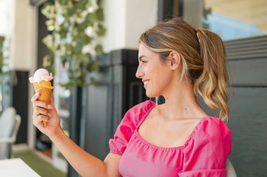 Açık havada kornet dondurmalı genç sarışın kadın, neşeli bir ifadeyle.
