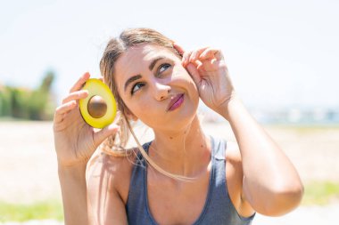 Avokado tutan genç sarışın bir kadın. Şüpheleri var ve kafası karışık.