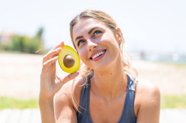 Avokado tutan genç sarışın kadın gülümserken yukarı bakıyor.